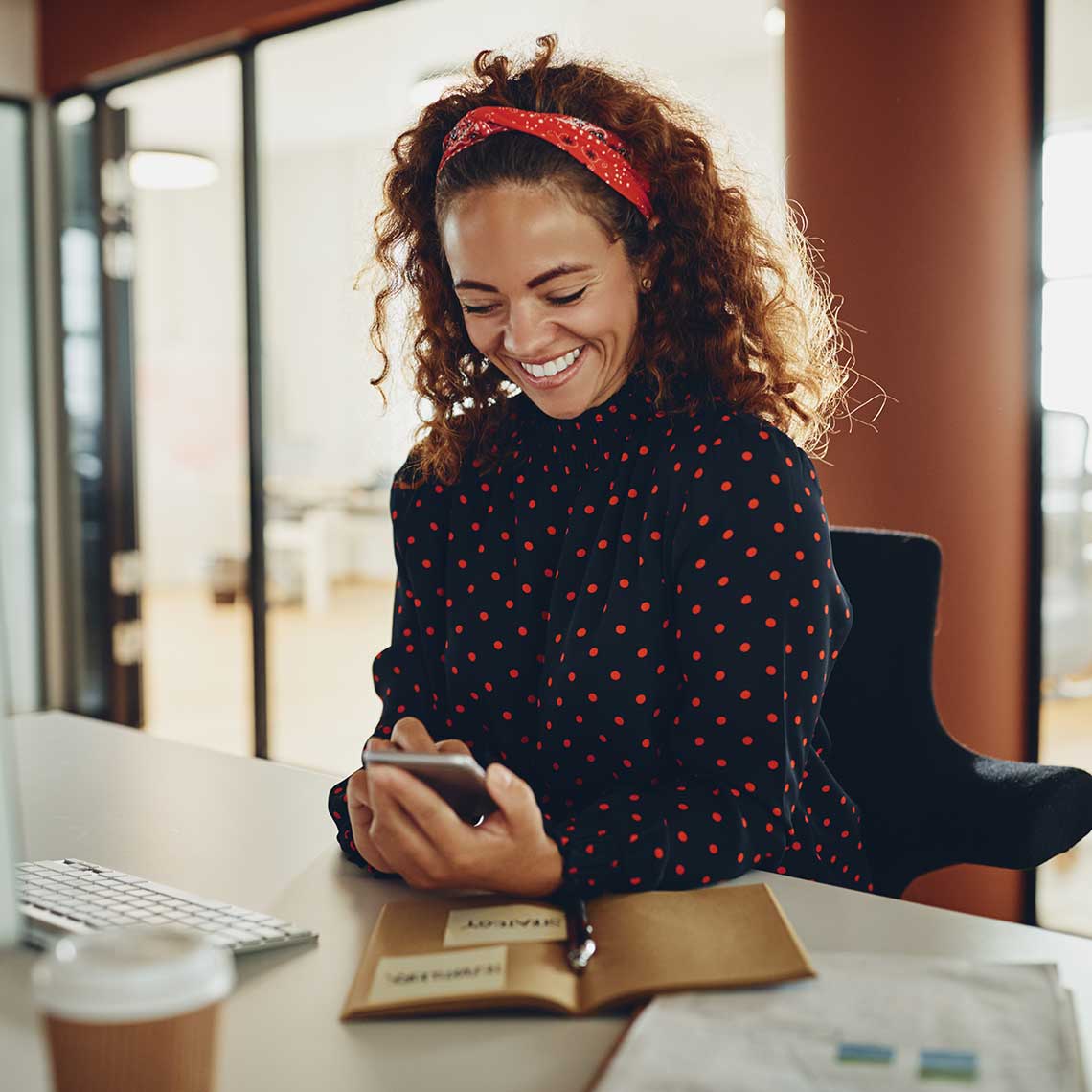 Woman smiling at her desk on her cell phone. Woman smiling at her desk on her cell phone.
