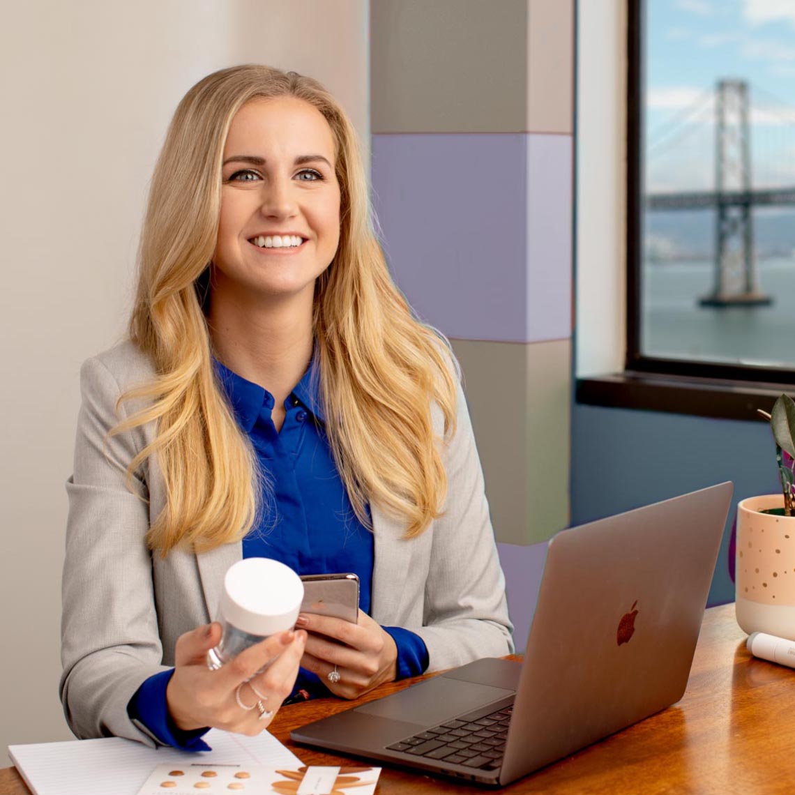 Woman holding R+F product and smiling in front of laptop. Woman holding R+F product and smiling in front of laptop.